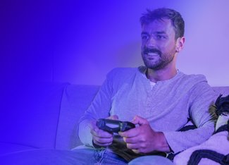 man sitting on a couch, smiling while playing a video game