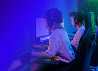 Two people with headphones are focused on their own PC