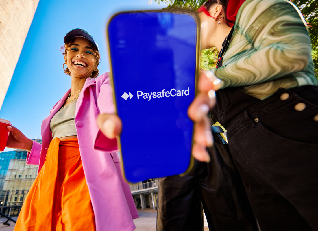 woman laughing and holding phone, which shows the PaysafeCard logo, into the camera.